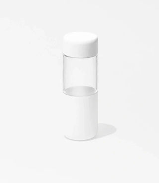 A clear cylindrical container with a white lid and white base, standing upright on a light gray background.