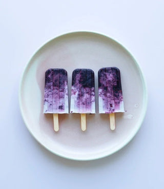 Three purple and white popsicles are arranged side by side on a round, light-colored plate, photographed from above against a white background.