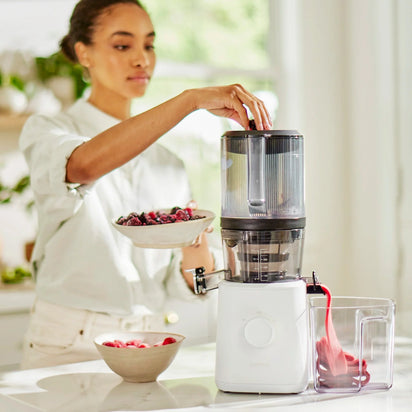 In a bright kitchen, someone adds berries to a juicer equipped with the Sorbet Attachment. Fresh juice flows from the spout into a container, while a bowl of berries sits nearby—creating a fresh and healthy scene that’s perfect for preparing homemade sorbet or another nutritious dessert.
