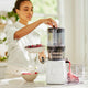 In a bright kitchen, someone adds berries to a juicer equipped with the Sorbet Attachment. Fresh juice flows from the spout into a container, while a bowl of berries sits nearby—creating a fresh and healthy scene that’s perfect for preparing homemade sorbet or another nutritious dessert.