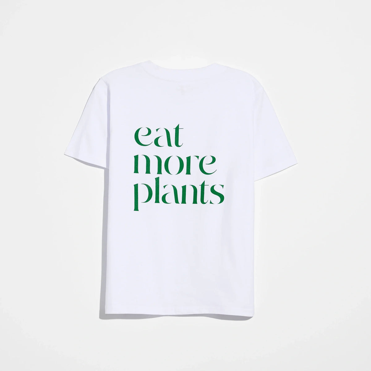 The Eat More Plants T-shirt is a relaxed fit tee crafted from 100% combed cotton for ultimate comfort. This white shirt features the phrase “eat more plants” printed in bold green letters on the back and is displayed against a plain white background.