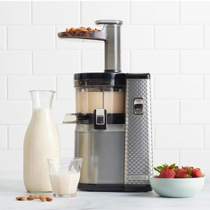 A silver and black Nama J1 Plug Type I cold press juicer sits on the counter with almonds being fed in. Nearby are a glass bottle and glass of almond milk, highlighting how easy it is to clean while making fresh, nutrient-rich juices.