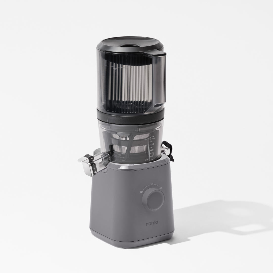 The Nama J2 is a modern gray cold press juicer with a transparent top section and front control dial, displayed on a white background.
