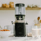 The Nama J2 Plug Type I, an easy-to-clean juicer for effortless meal prep, sits beside a blender with a bowl of food and glasses of milk.