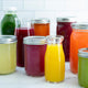 An array of vibrant juices in clear bottles is displayed on a white surface with a tiled backdrop—great inspiration for Juicing for Beginners or anyone exploring plant-based recipes.
