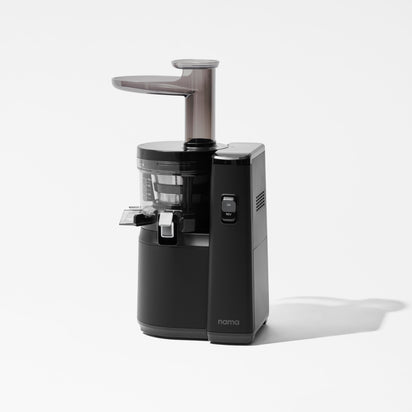 The Nama J1 is a sleek, modern black cold press juicer with a transparent section and side spout, displayed on a plain white background. The nama logo appears on the front, ideal for preparing nutrient-rich juices.