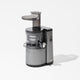 The Nama J1 is a modern cold press juicer in silver and black, featuring a transparent chamber and dark top chute, designed for easy cleaning and making nutrient-rich juices. Shown against a plain white background.