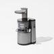 The Nama J1, a modern silver and black cold press juicer with a transparent container and vertical feeding tube for nutrient-rich juices, is displayed on a plain white background.