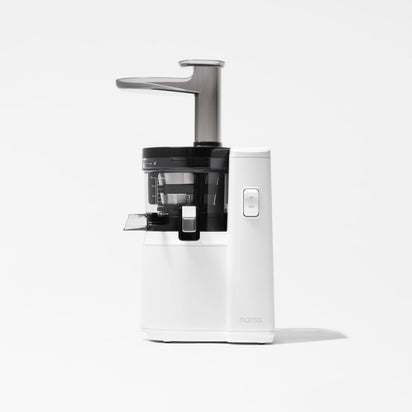 The Nama J1 is a modern cold press juicer in white and black with a transparent chamber, spout, and vertical feeding tube—designed for nutrient-rich juices and easy cleaning, shown against a plain white background.