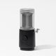 The Nama M1 Plug Type I is a modern, black and transparent plant-based milk maker with a cylindrical design, round dial, and side spout, shown on a white background.