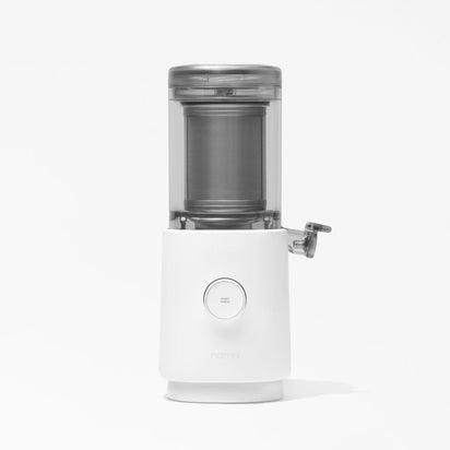 The Nama M1 Plug Type E is a modern, white countertop cold press juicer with a transparent top, cylindrical chamber, silver side spout, and central power button—ideal for plant-based milk—shown against a plain white background.