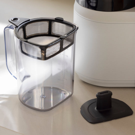 The Nama Pulp Strainer for J1 & C2 sits next to a white appliance and a black silicone lid on a light countertop.