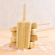 Six popsicles made with the Nama Popsicle Mold are stacked in a pyramid, wooden sticks pointing outward, and rest on scattered ice cubes atop a peach-colored surface.