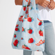 A person holds the Nama + Baggu Standard Tote Bag, featuring a blue background with a red strawberry print.