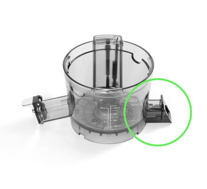 Transparent plastic food processor bowl with measurement markings and spout, shown on white. A green circle highlights the black locking tab (right side)—compatible with cold press juicers using the Pulp Outlet Loop.