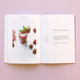 An open recipe book on a pink surface shows a vibrant photo of a pink smoothie garnished with mint and strawberries, surrounded by fresh berries—its “Berry Mint Burst” recipe features Juice the Rainbow for plant-based nutrition.