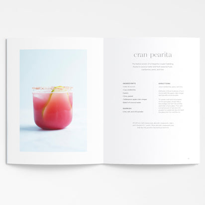 An open copy of "A Collection of Holiday Recipes" shows a photo of a pink cocktail with a lemon twist on one page and the cran pearita healthy holiday mocktail recipe with ingredients and instructions on the opposite page.