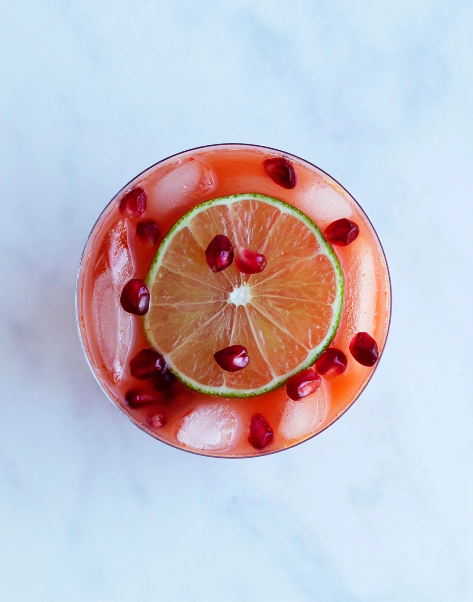 A pink cocktail in a glass topped with a lime slice and pomegranate arils.
