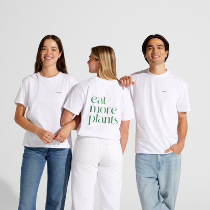 Three people stand together in white jeans and Eat More Plants T-shirt. The person in the middle, wearing a relaxed fit 100% combed cotton tee, faces away to display "eat more plants" as the others smile at the camera.