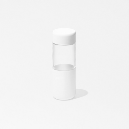 The On-the-Go Glass Bottle features a minimalistic, clear design with white caps on the top and bottom—perfect for juice while out and about. Photographed against a plain white background.